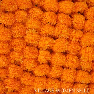 May include: A close-up image of a large quantity of bright orange marigold flower heads. The flowers are arranged in a dense, textured pattern, creating a vibrant and colorful background. The text "VILLAGE WOMEN SKILL" is visible at the bottom of the image.