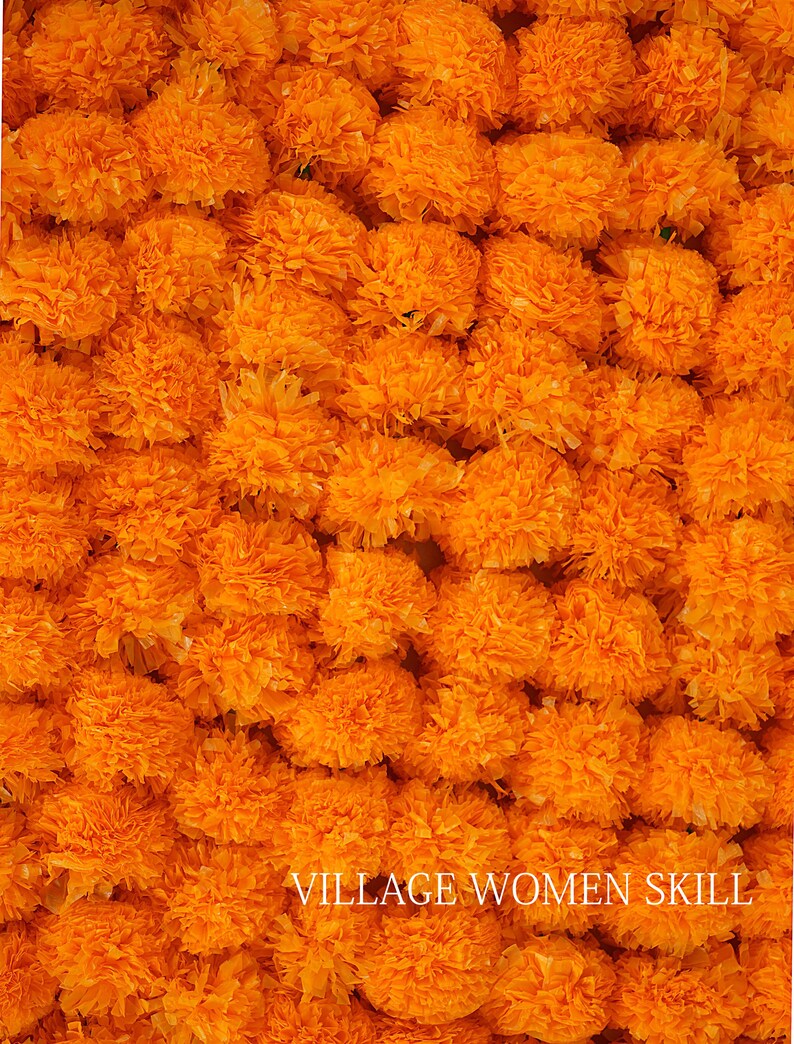 May include: A close-up image of a large quantity of bright orange marigold flower heads. The flowers are arranged in a dense, textured pattern, creating a vibrant and colorful background. The text "VILLAGE WOMEN SKILL" is visible at the bottom of the image.