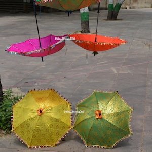 K&ouml;nnte beinhalten: Eine Sammlung farbenfroher, dekorativer Sonnenschirme. Die Schirme sind in Pink, Orange, Gr&uuml;n und Gold gehalten. Jeder Schirm hat eine dekorative Bord&uuml;re und Quastenfransen. Einige Schirme sind aufgeh&auml;ngt.