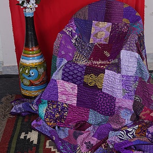 May include: A purple and pink patchwork quilt made from recycled saris. The quilt is folded and draped over a chair. The text "Village Women Skill" is visible on the quilt.