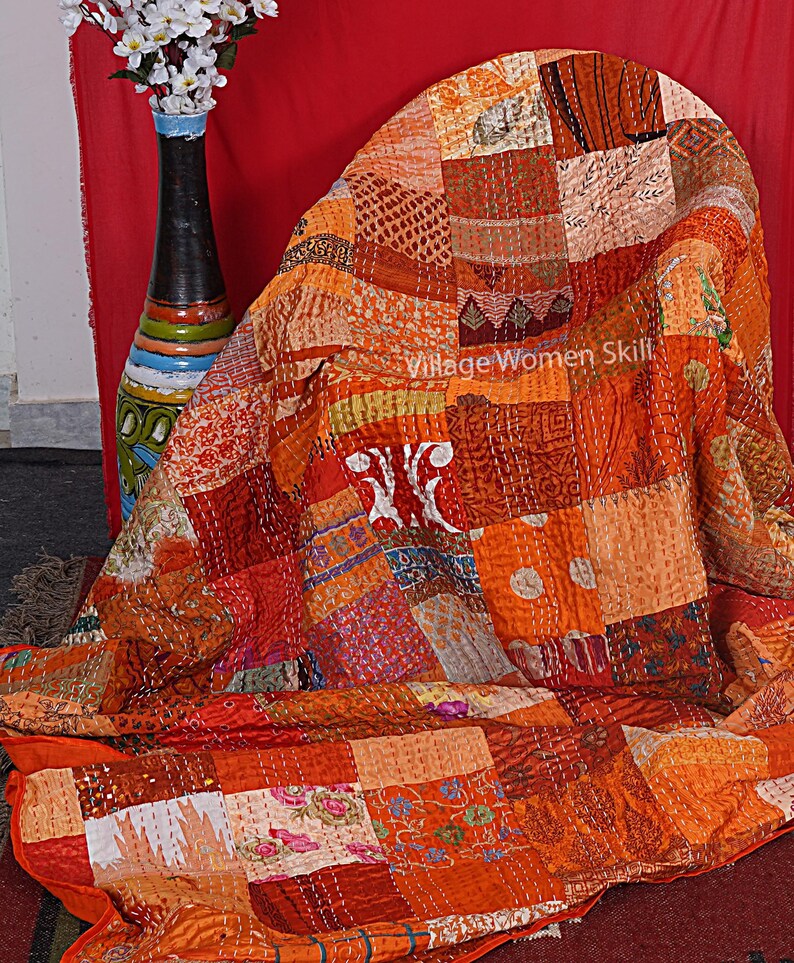 May include: A patchwork quilt made of various fabrics in shades of orange, red, and brown. The quilt is hand-stitched and has a unique, rustic look. "Village Women Skill" is written on the quilt.