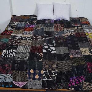 May include: A black kantha quilt with a patchwork design featuring various patterns and colors. The quilt is made of recycled saris and is hand-stitched. The quilt is laid out on a bed with two white pillows.