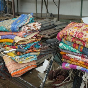 Puede incluir: Una pila de colchas kantha de colores est&aacute; atada a una bicicleta, con otra pila de colchas en el suelo junto a ella. Las colchas est&aacute;n hechas de algod&oacute;n y tienen una variedad de patrones y colores.