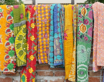 May include: A collection of colorful kantha quilts hanging on a brick wall. The quilts are made of recycled saris and feature a variety of floral and geometric patterns.