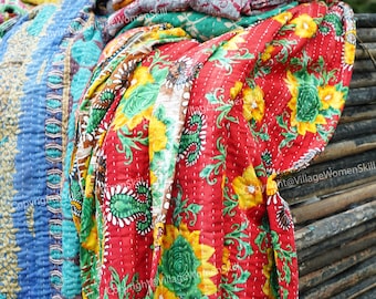 May include: A stack of colorful kantha quilts with floral patterns. The quilts are made of recycled saris and are hand-stitched. The quilts are folded and stacked on top of each other. The quilts are a vibrant mix of colors, including red, yellow, blue, green, and pink.