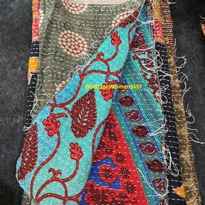 May include: A stack of colorful fabric squares with intricate patterns, stitched together with white thread. The fabric is a mix of green, blue, red, and black. The fabric is frayed at the edges, giving it a vintage look.  @VillageWomensSkill