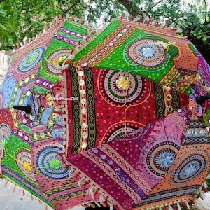 May include: Two colorful, patterned umbrellas with intricate designs. The umbrellas feature a mix of red, green, blue, and purple fabrics with circular and geometric patterns. Each umbrella has a black handle and decorative fringe.