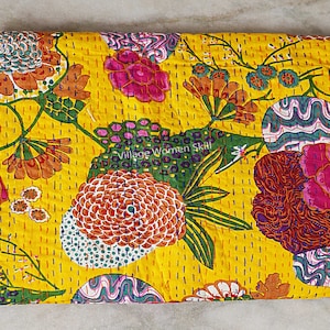 May include: A yellow kantha quilt with a floral pattern in shades of pink, red, green, and blue. The quilt is hand-stitched and has a "Village Women Skill" label.