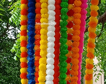 Könnte beinhalten: Eine Sammlung bunter Girlanden aus Pompons. Die Girlanden bestehen aus blauen, orangen, gelben, weißen, grünen und rosa Pompons. Die Girlanden hängen an einem Baumzweig. "Village Women Skill" steht auf einem weißen Etikett.
