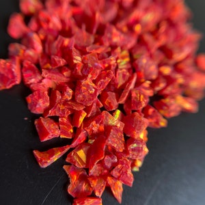 May include: A pile of red iridescent glass chips. The chips are irregular in shape and have a shimmering, rainbow-like effect.