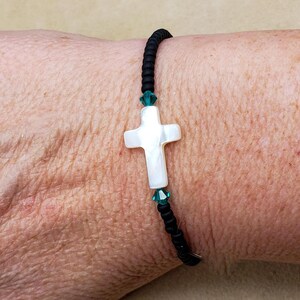 May include: A black beaded bracelet with a white mother-of-pearl cross charm and green crystal accents.