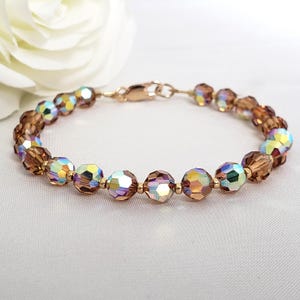 May include: A bracelet featuring faceted, iridescent brown crystal beads with a metallic finish, interspersed with small gold-toned metal spacer beads. The piece is secured with a gold-toned metal lobster claw clasp, creating a circular design.