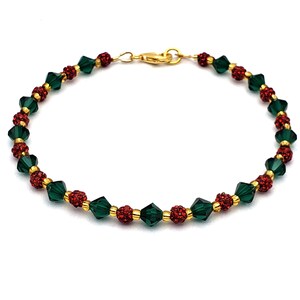 May include: A gold-toned bracelet featuring alternating dark green faceted beads and clusters of red, sparkling beads. The bracelet is strung on a gold chain and has a lobster clasp.