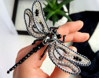 May include: A black and white beaded dragonfly brooch with a large black rhinestone in the center. The wings are made of delicate lace and beads.