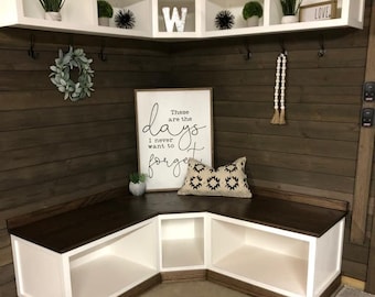 May include: A white corner bench with a dark brown wood top and three open shelves. The bench is in a room with a wood wall and white shelves with decorative items. A sign on the wall reads "These are the days I never want to forget".