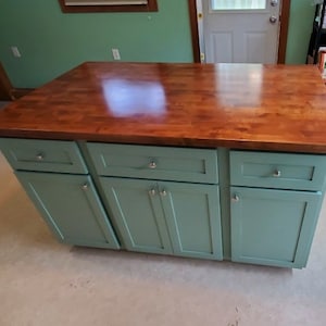 May include: A kitchen island with a wood countertop and teal cabinets. The island has three drawers and three doors. The countertop is smooth and shiny.