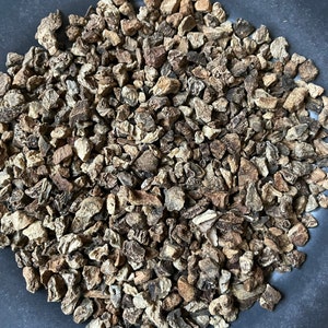 May include: A close-up view of a bowl filled with dried burdock root pieces. The pieces are a light brown color and have a rough texture.