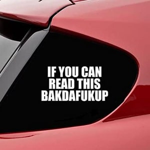 May include: A red car with a black window featuring a white decal. The decal reads "IF YOU CAN READ THIS BAKDAFUKUP" in a bold, sans-serif font. The image is a close-up of the car's exterior.