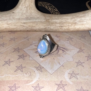 May include: A silver ring with a teardrop-shaped iridescent opal stone set in a detailed silver bezel.