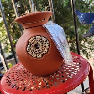 May include: Terracotta hanging planter with a rope handle and a decorative ceramic medallion with the words "Under the Coco Pot".