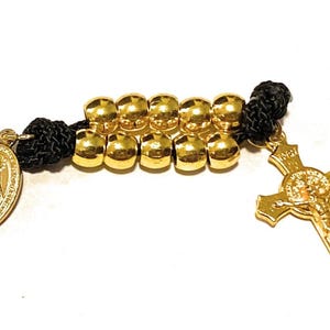 May include: Gold rosary beads with a black cord, a gold cross with a figure of Jesus Christ, and a gold medal with an image of the Virgin Mary.