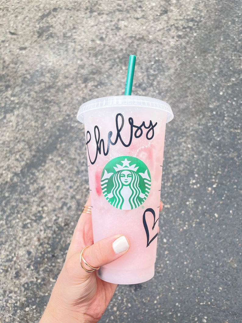 Starbucks cold venti cup, filled with pink drink.  Custom name personalized on the outside above the Starbucks logo and the outline of a heart below the logo.  Cute coffee cup gift for her.