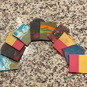 May include: A collection of handmade soap bars in various colors and patterns, including blue, green, red, yellow, and black. The bars are arranged in a semi-circle shape.