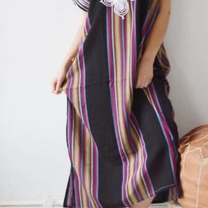 May include: A long, black and white striped dress with a white embroidered design on the chest. The dress has short sleeves and a loose fit.