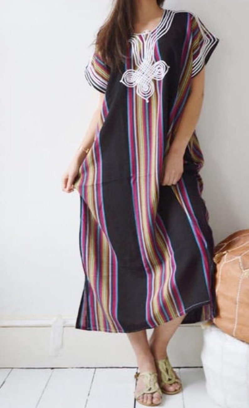 May include: A long, black and white striped dress with a white embroidered design on the chest. The dress has short sleeves and a loose fit.