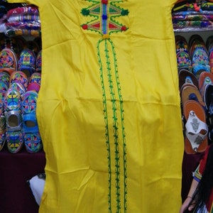 May include: A yellow long-sleeved dress with green and red embroidery. The dress has a V-neck and a long skirt. The embroidery is intricate and colorful.
