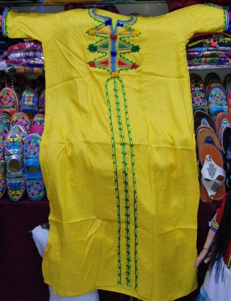 May include: A yellow long-sleeved dress with green and red embroidery. The dress has a V-neck and a long skirt. The embroidery is intricate and colorful.