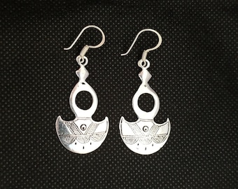 May include: A pair of silver earrings with a unique design. Each earring features a crescent moon shape with intricate details and a small circle in the center.