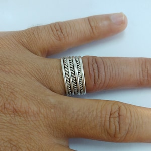May include: A silver ring with a braided design. The ring is worn on a finger.