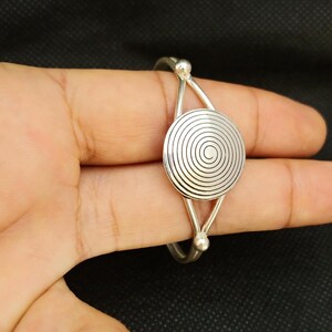 May include: Silver bangle bracelet with a spiral design. The bracelet is open and has a circular design with a spiral pattern.