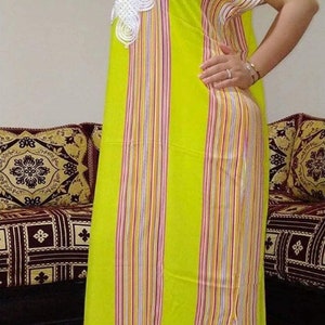 May include: A long, yellow and white striped dress with a white lace design on the neckline. The dress has a side slit and is made of a lightweight fabric.