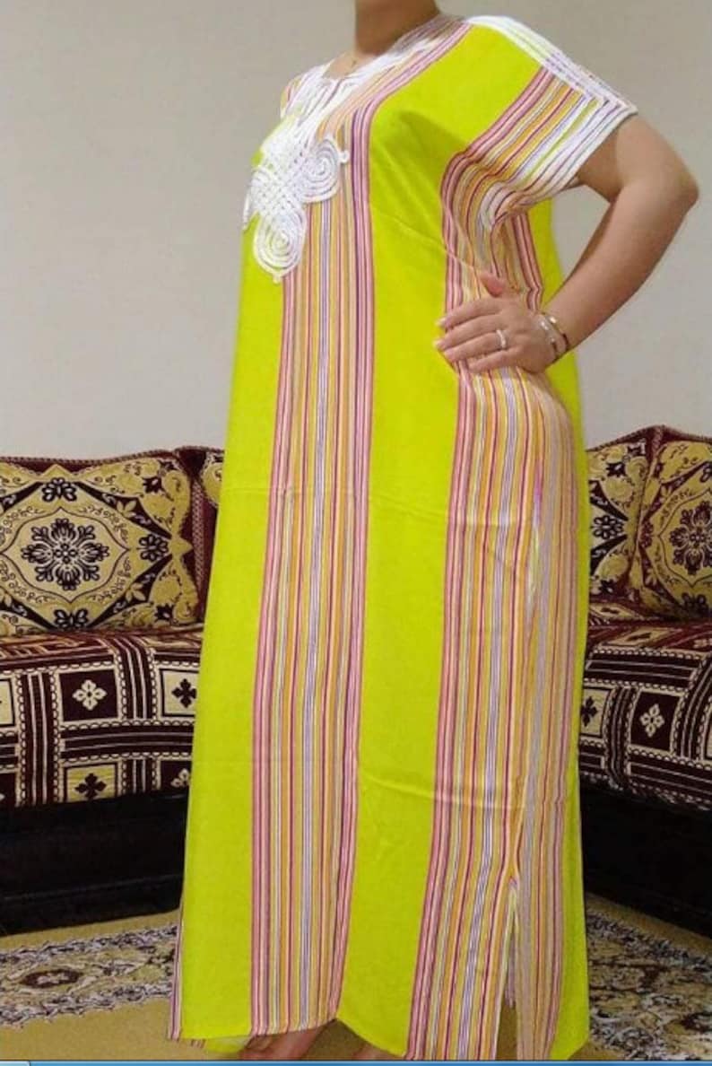 May include: A long, yellow and white striped dress with a white lace design on the neckline. The dress has a side slit and is made of a lightweight fabric.