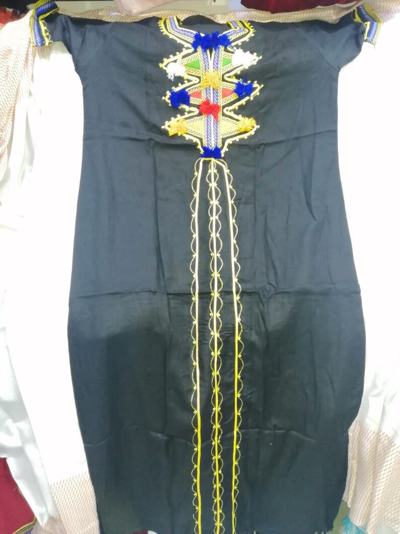 May include: A black long-sleeved dress with a colorful embroidered design on the neckline. The embroidery features geometric shapes, tassels, and pom-poms in shades of blue, red, green, and yellow. The dress has a long, flowing skirt and a fitted bodice.