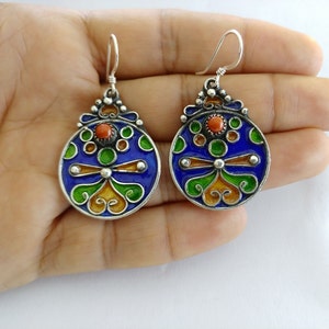May include: A pair of silver earrings with blue, green, orange, and red enamel. The earrings are round and have a floral design.