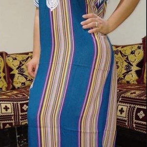 May include: A long, blue and white striped dress with a white crocheted design on the neckline. The dress has short sleeves and a loose fit.