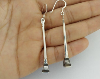 May include: A pair of silver dangle earrings with a geometric design. The earrings are long and slender, with a black and silver striped detail at the bottom.