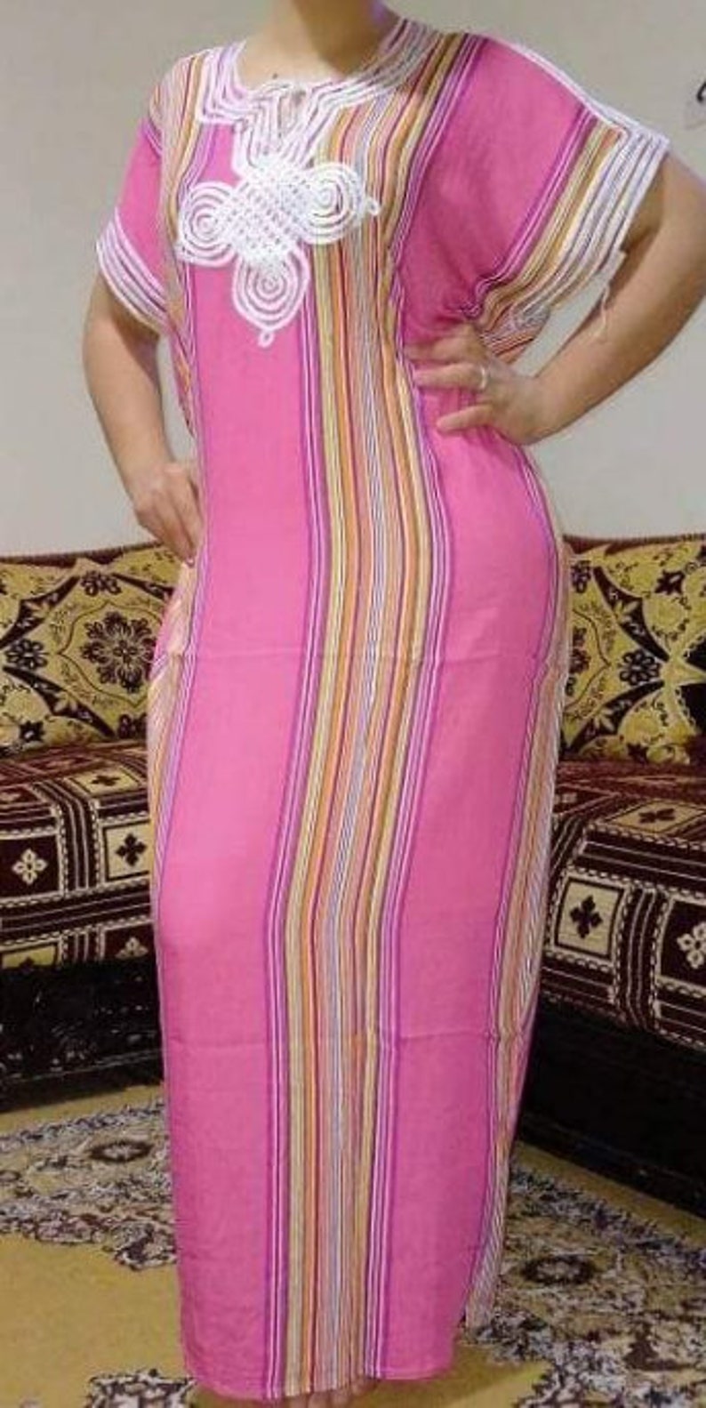 May include: A pink and white striped dress with a white crocheted design on the neckline. The dress has short sleeves and a long, flowing skirt.