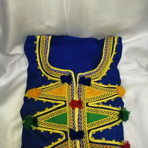 May include: A blue garment with intricate gold embroidery and colorful pom-poms. The garment features a geometric pattern with triangles and zigzags.