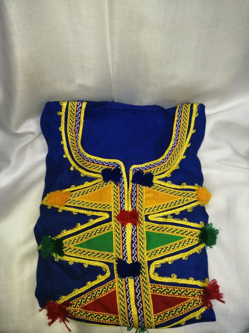 May include: A blue garment with intricate gold embroidery and colorful pom-poms. The garment features a geometric pattern with triangles and zigzags.
