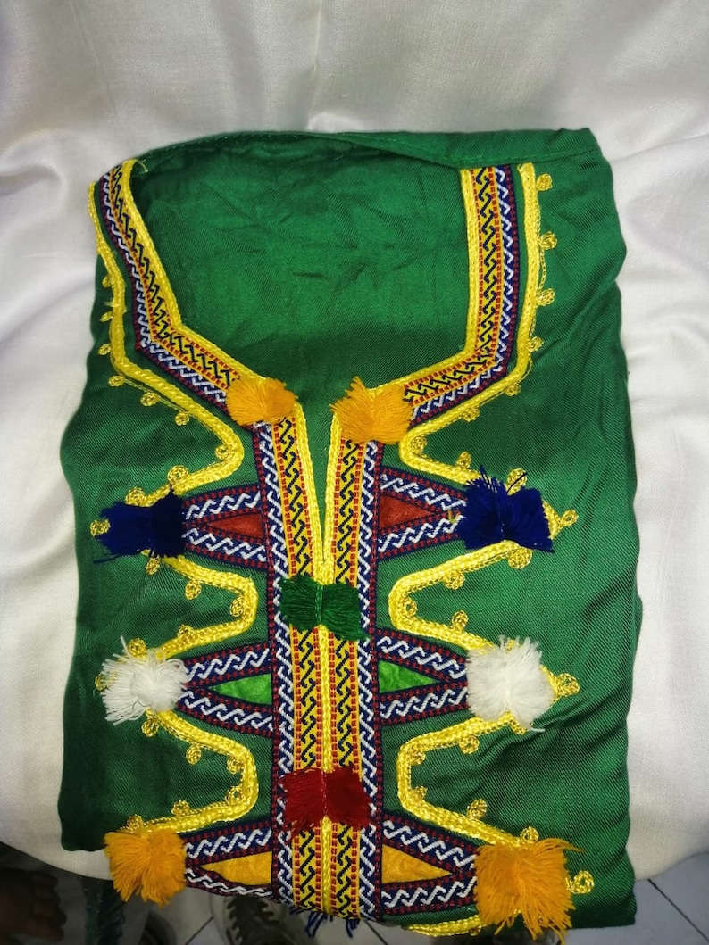May include: A green garment with intricate embroidery featuring yellow, red, blue, and white thread. The garment has a high neckline and is adorned with colorful tassels.