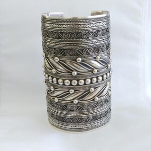 May include: A silver cuff bracelet with intricate designs and beaded accents. The bracelet is wide and has a textured surface.