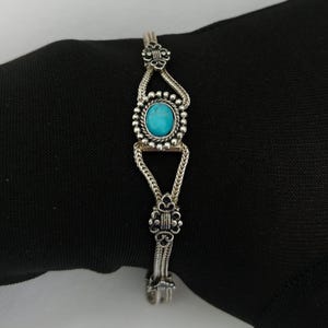 May include: A silver bracelet with a turquoise stone set in a decorative silver frame. The bracelet has a chain link design with decorative accents.