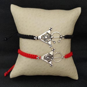 May include: Two bracelets with silver triangle charms. One bracelet has a black cord and the other has a red cord.