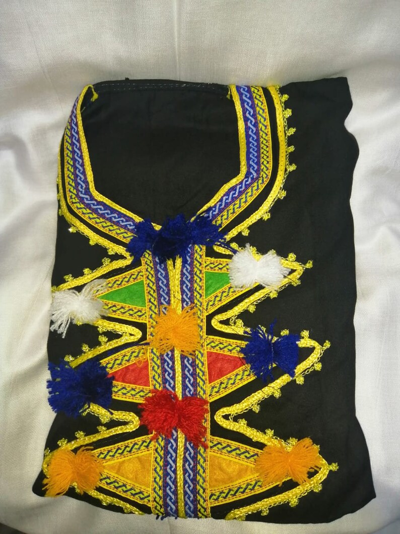 May include: Black garment with intricate embroidery featuring yellow, blue, red, and white pom-poms. The neckline is adorned with a decorative trim in blue and yellow.