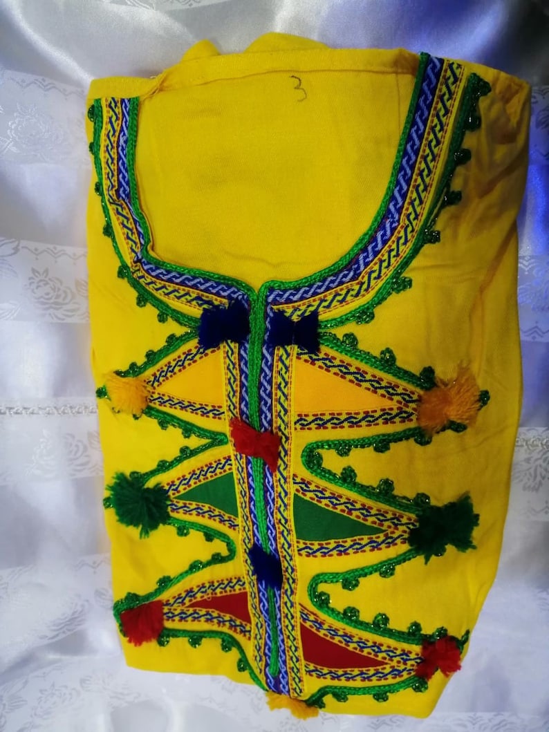 May include: Yellow fabric top with colorful embroidery and pom-poms. The embroidery features geometric shapes and a variety of colors, including red, green, blue, and yellow.