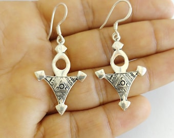 May include: A pair of silver earrings with a geometric design. The earrings are in the shape of a triangle with a circle in the center. The earrings are hanging from a hook.